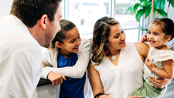 A dentist at Community Dental Partners greets a mother and her children at the front desk.