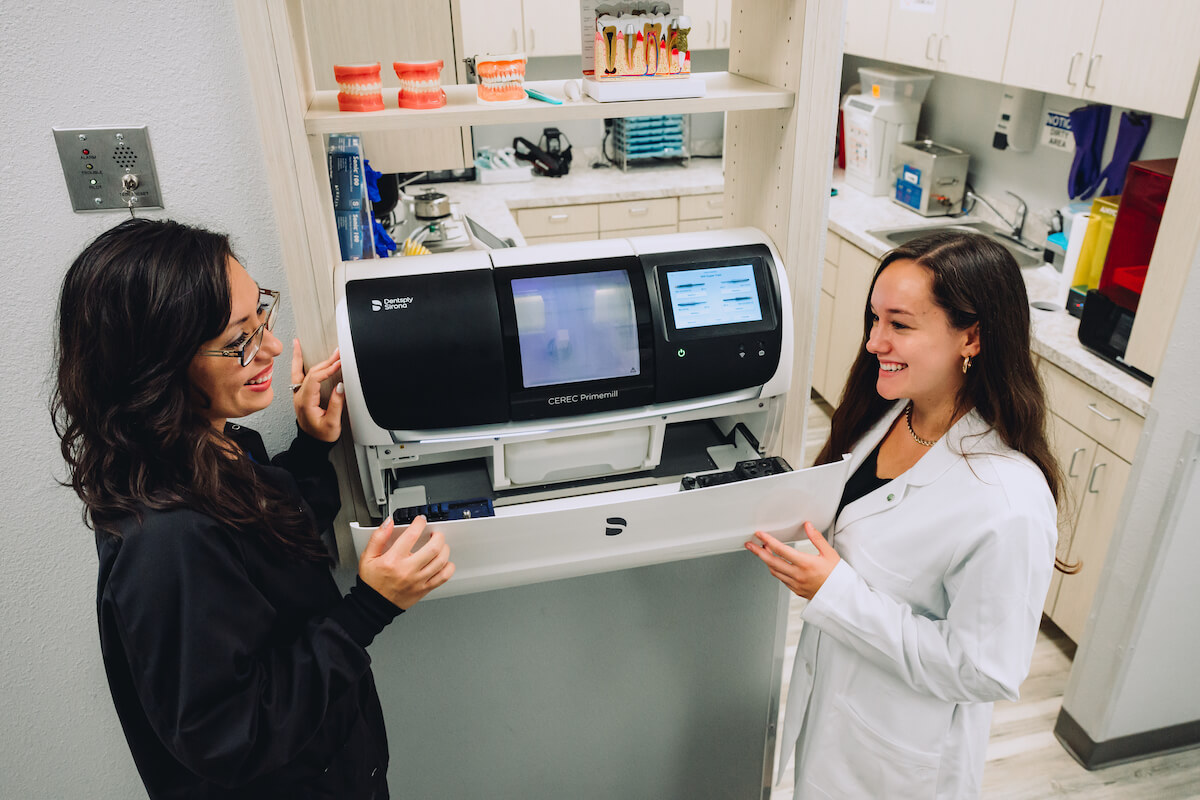 A dentist listens to her mentor explain how to use the machinery in their dental practice.