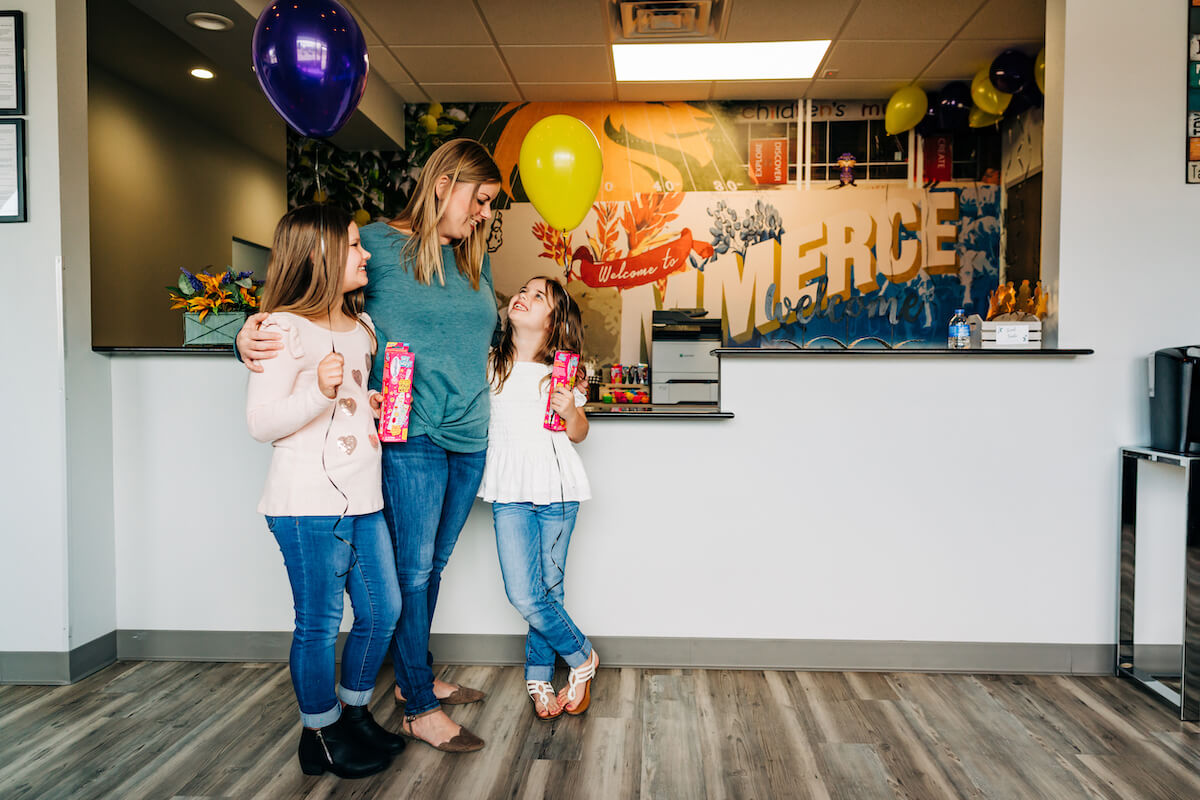 A mother stands with her daughters at the dentist after a checkup. Dental care in underserved communities is incredibly important to our mission.