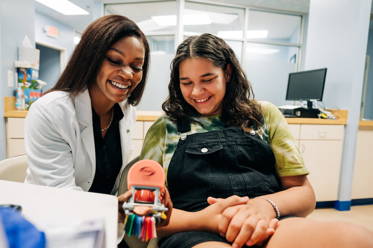 Orthodontist showing young female patient what braces would look like on a model set of teeth.