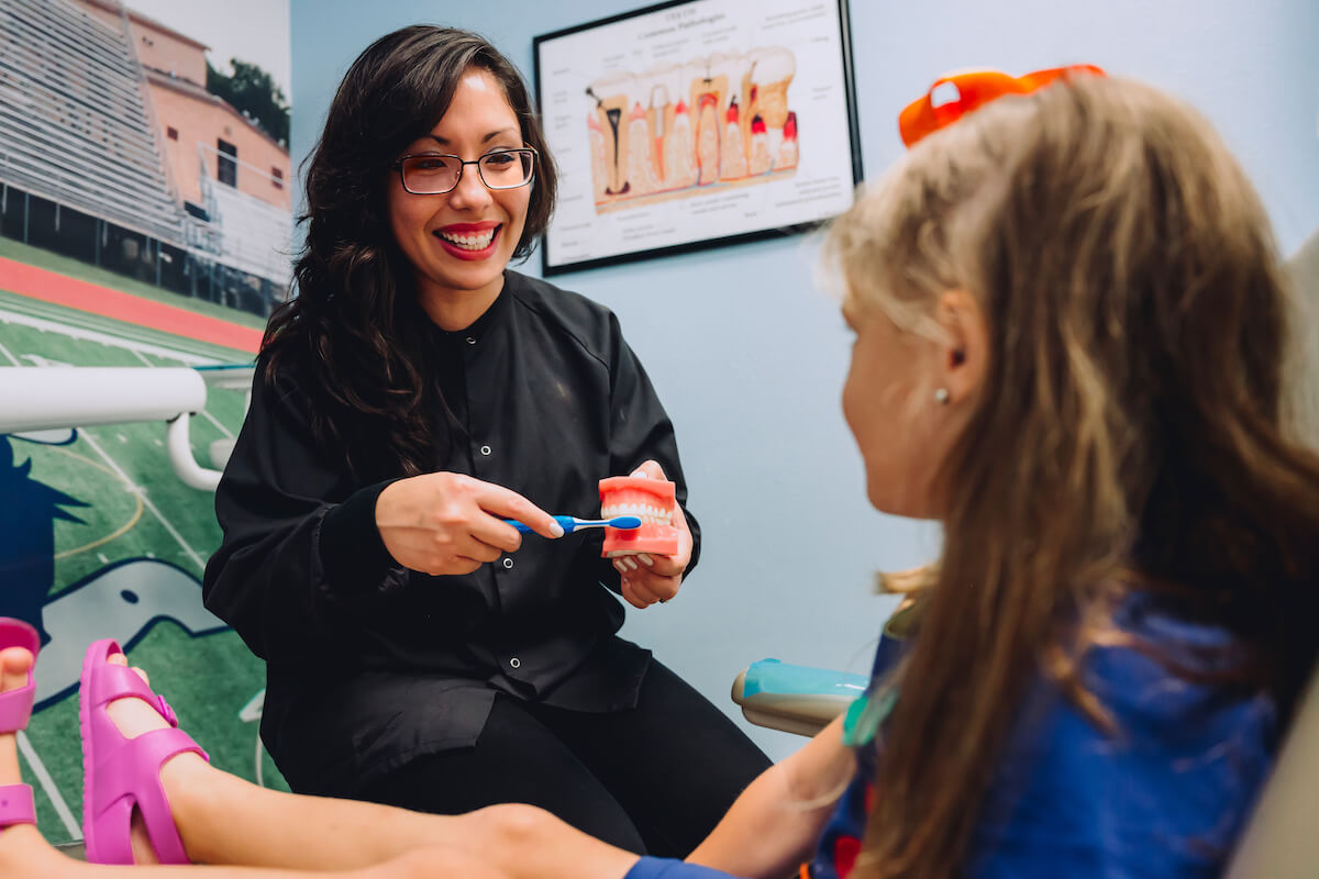 CDP dentist showing young child patient how to brush teeth on a fake set of teeth