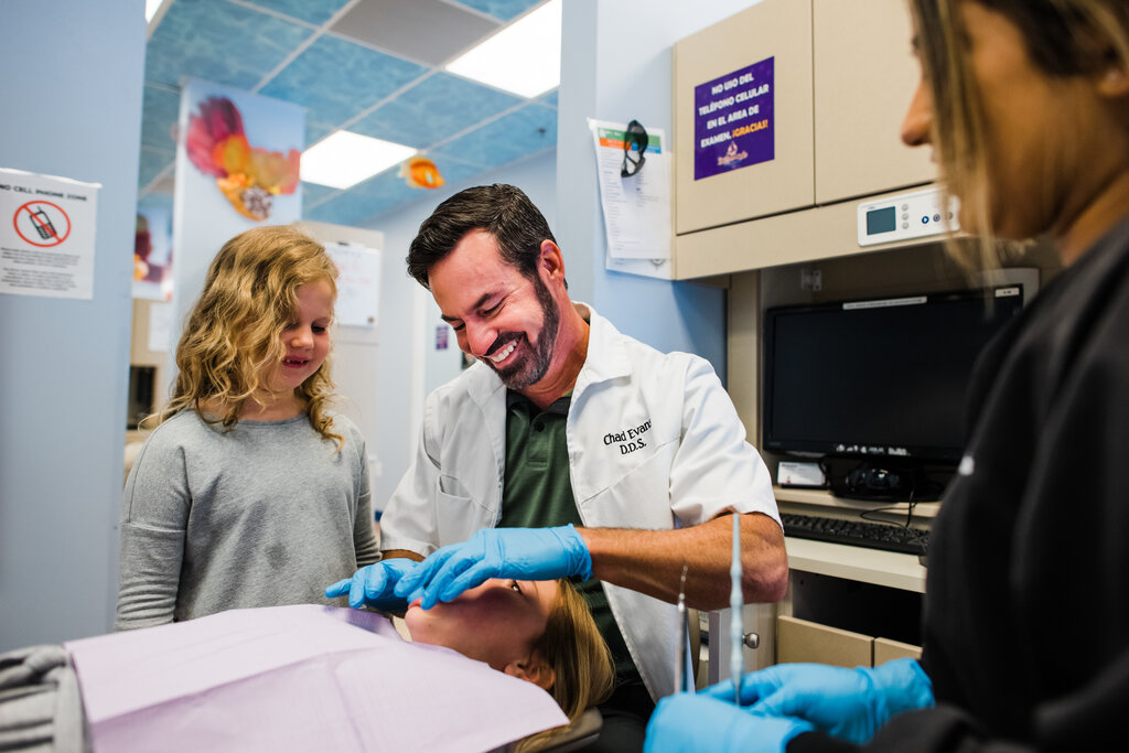 Dentist working on patient with young child observing.