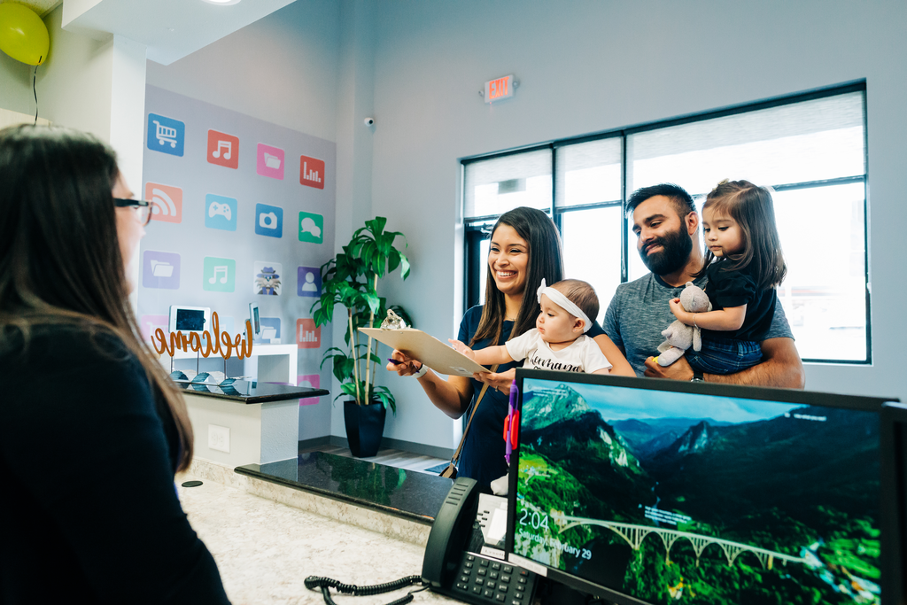 Family with young children turning in dental paperwork at front desk.