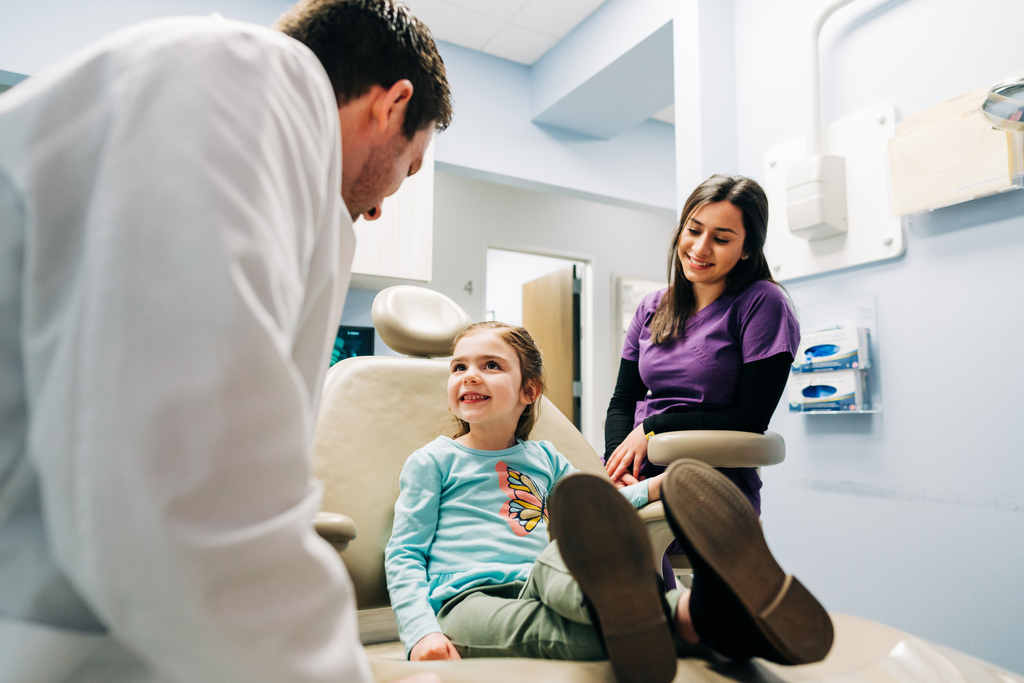 Dentist and hygienist smiling at a young female patient. 