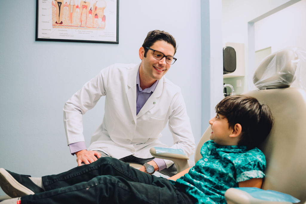 Part-time dentist smiling at young patient chairside. For dentists who choose to practice somewhere with a relatively low cost of living, like a rural community, part-time work may offer a high enough salary to give them the income they need and the free time they want.